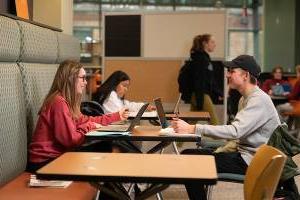 两个学生面对面坐在一张桌子旁，微笑着打开笔记本电脑